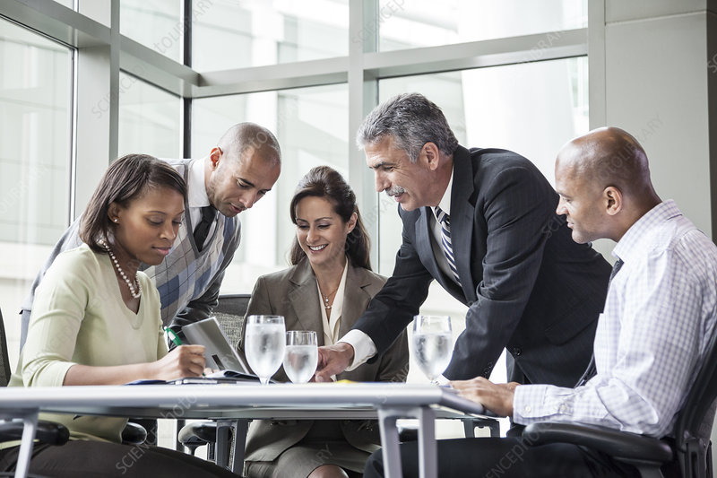 Group of male and female business people in a meeting at a conference table next to a large window in a convention centre.